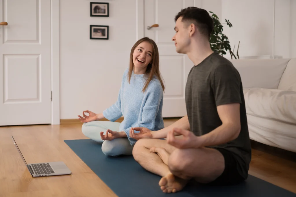A beautiful couple practicing yoga together at home while following an online yoga class on their laptop
