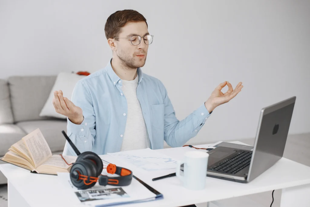 A man meditating in his office, sitting on a chair with his eyes closed and a calm posture.