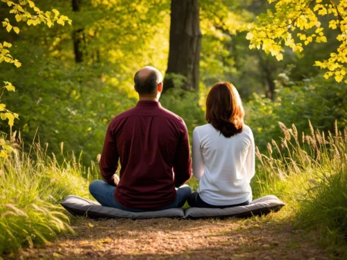 A couple meditating on the forest floor surrounded by lush green trees