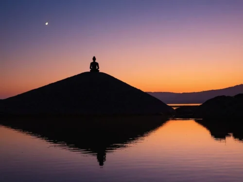 Woman sitting in meditation pose on beach sand dune during sunset with ocean horizon in background