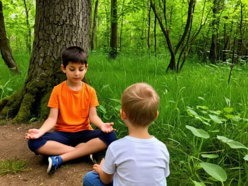 Two children sitting under tree on grass practicing meditation together outdoors