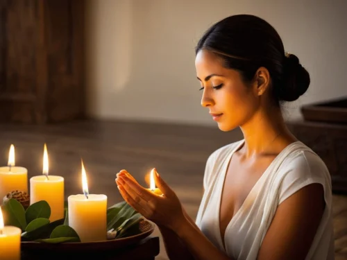 Woman in prayer holding lit candle in her hands during spiritual ritual