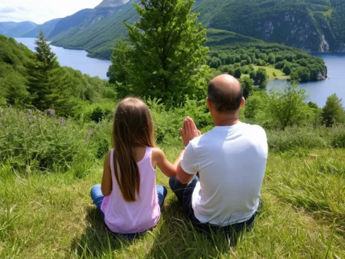Man and his young daughter kneeling in mindful prayer on a mountain overlooking a lake