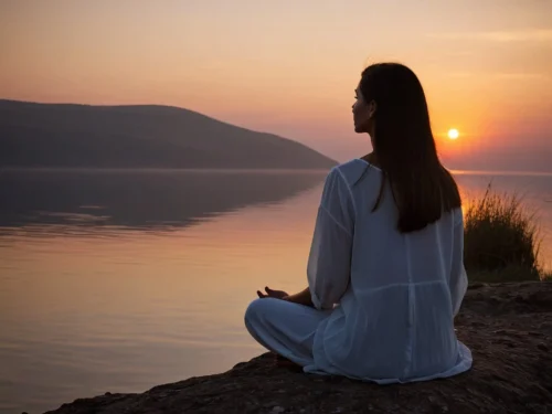 A solitary woman in deep meditation on a terrace overlooking a lake, watching the sunset.