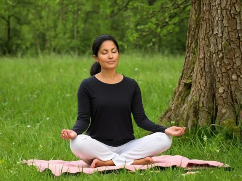 A solitary woman seated on the ground in meditation beneath a large tree.